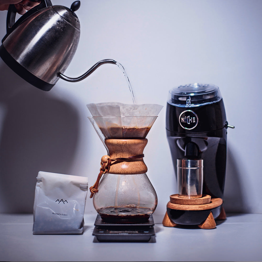 Black Niche Zero next to goose neck kettle pouring water into chemex