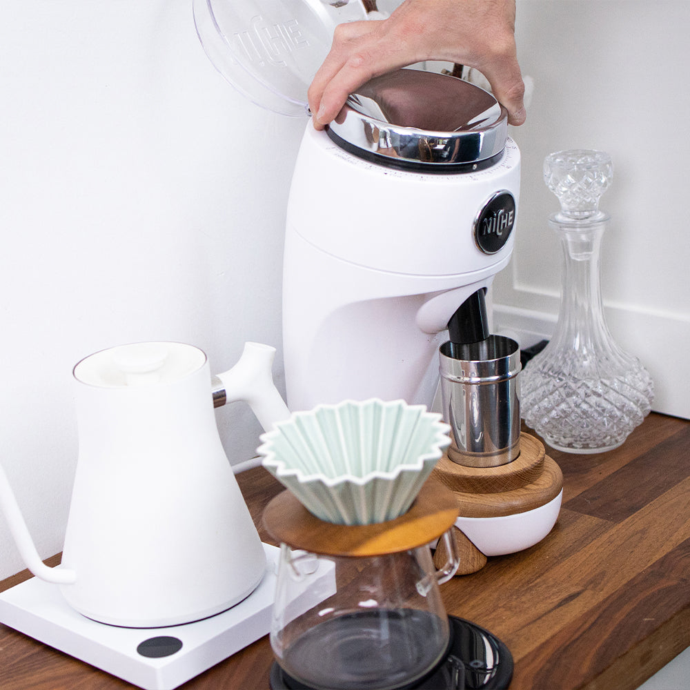 Adjusting grind setting on White Niche Duo next to pourover equipment