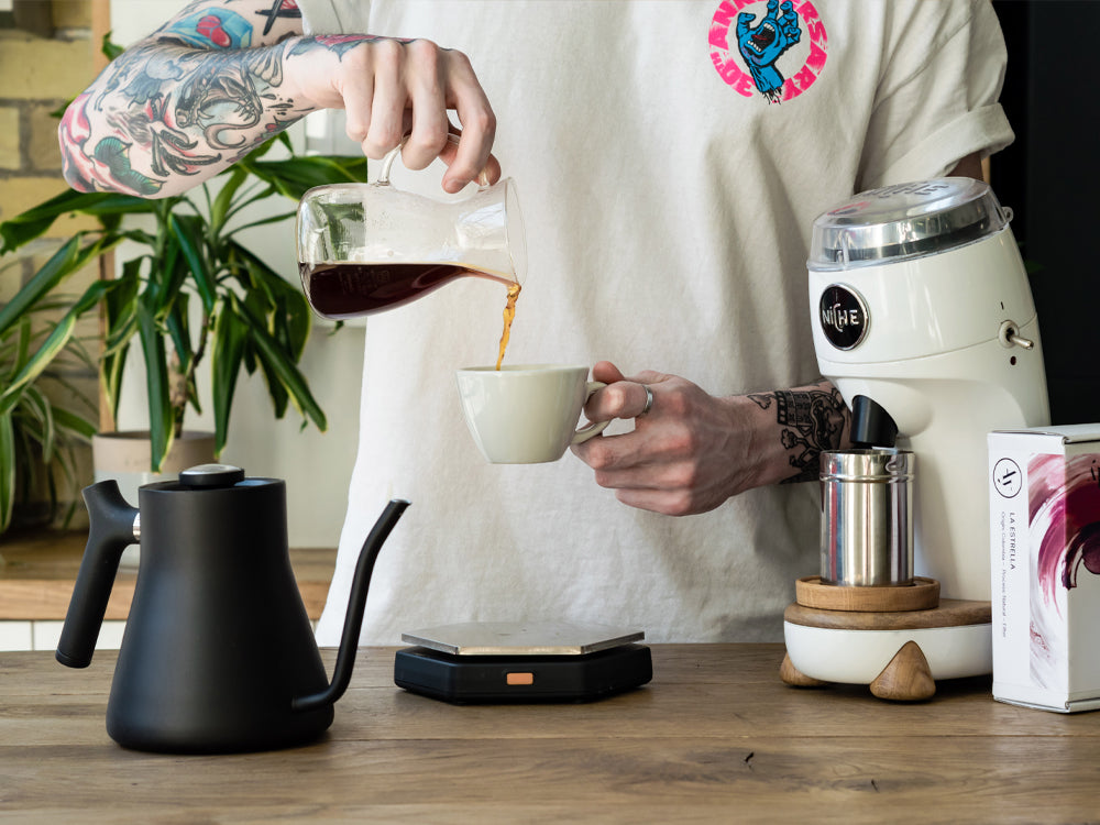 Man pouring freshly brewed pourover into mug next to White Niche Zero